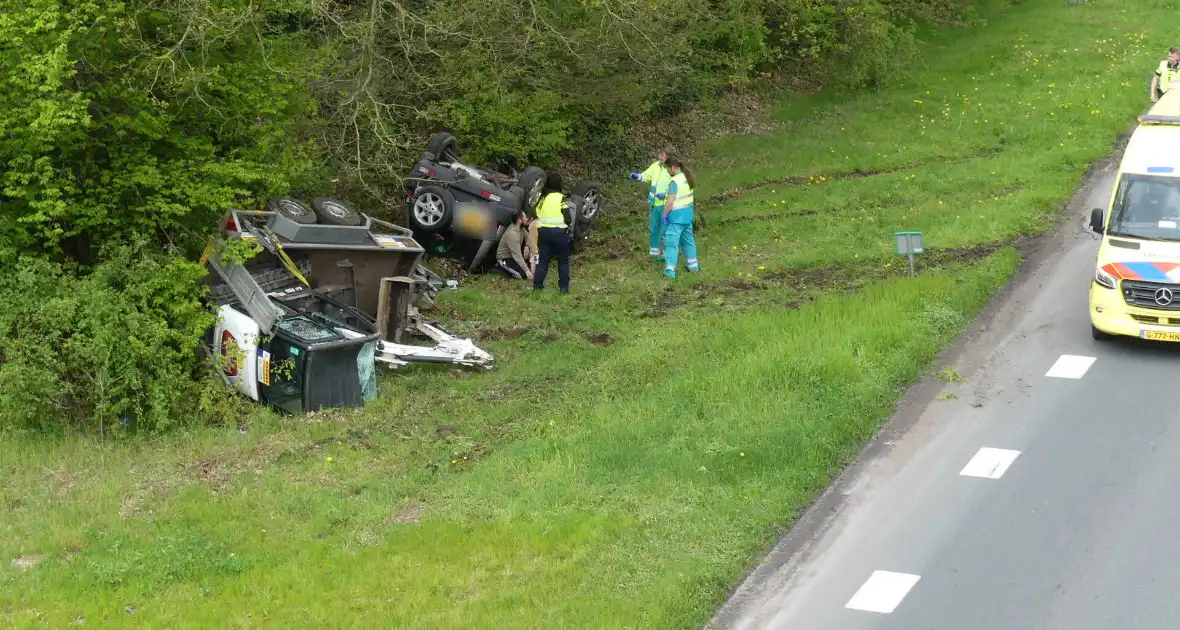 Auto en aanhanger met graafmachine over de kop