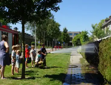 Kinderen blussen met brandweer brandende coniferenhaag