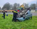 Auto belandt op kop naast rotonde