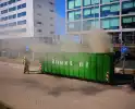 Vlammen slaan uit grote afvalcontainer