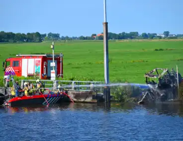 Tractor brandt uit langs waterkant, blusboot ingezet