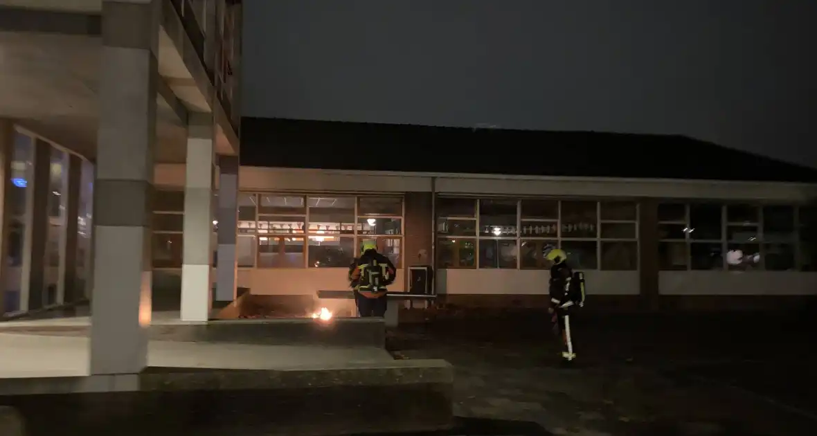 Brandweer blust brandende hoop kranten op schoolplein