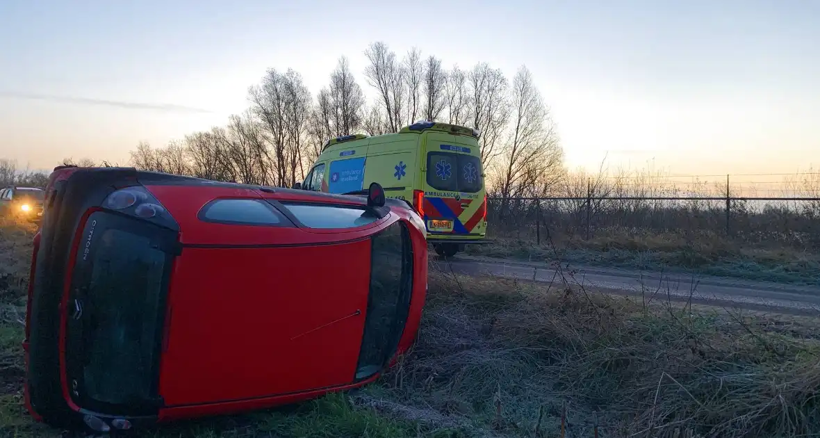 Auto belandt op zijn kant langs spekgladde weg